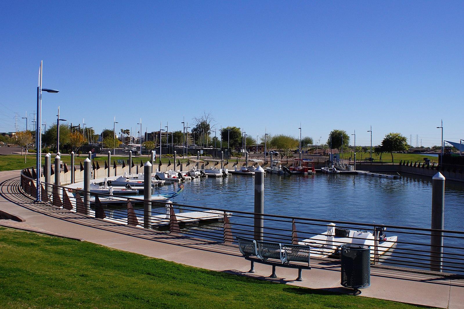 Sunny marina with many small boats docked along a curved walkway.