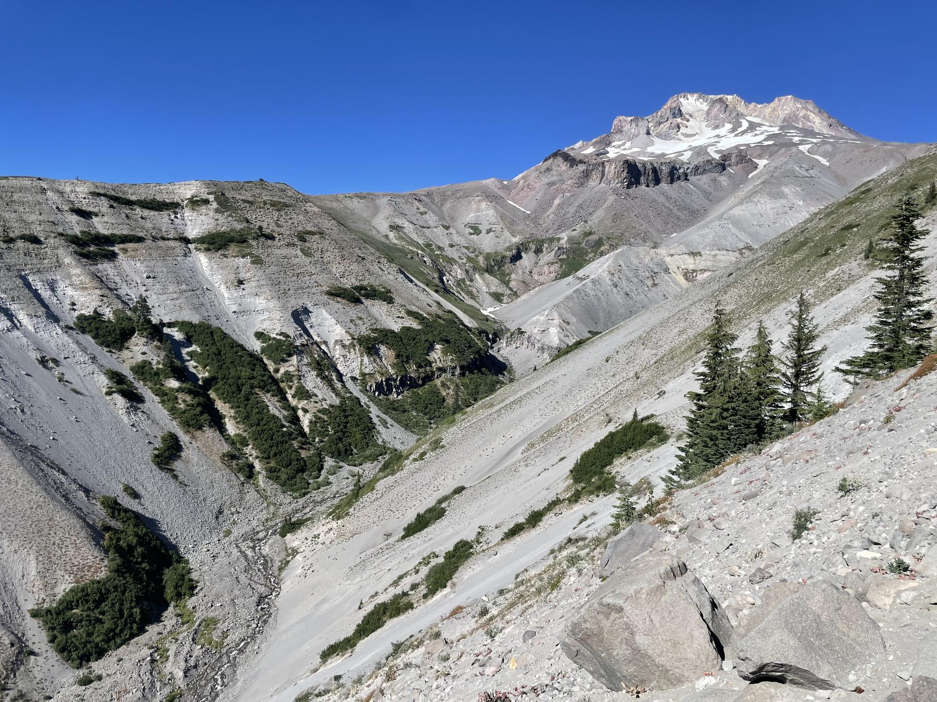 Expansive, steep rocky valley with a distant snow-capped mountain on a clear day.