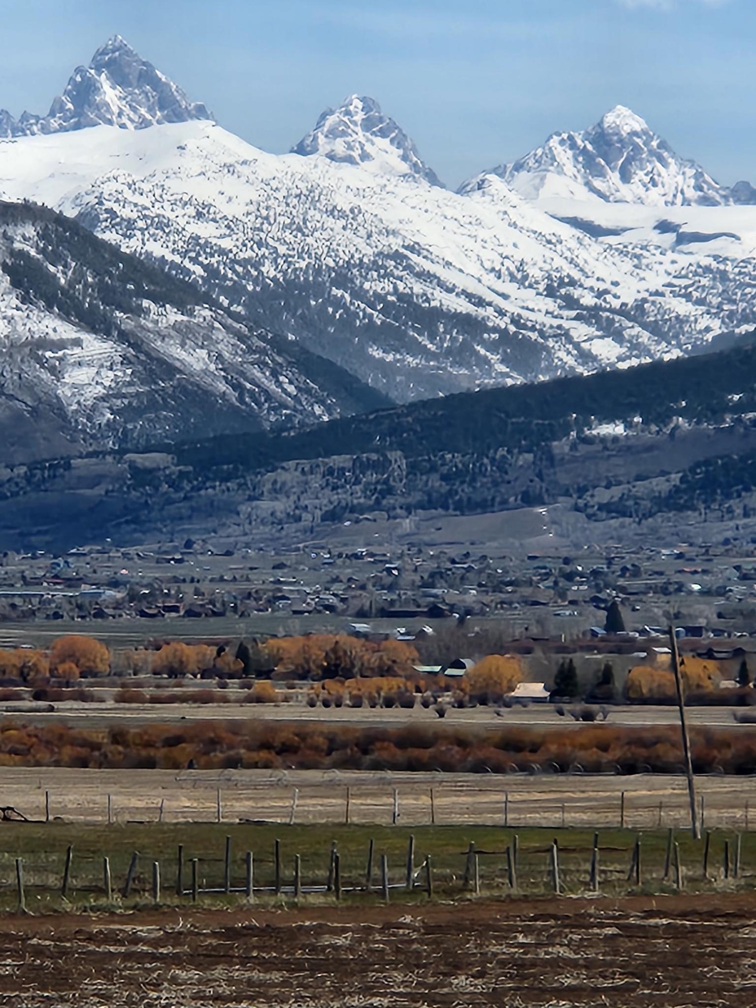 Majestic snow-capped mountains rise above a valley with fields and buildings.