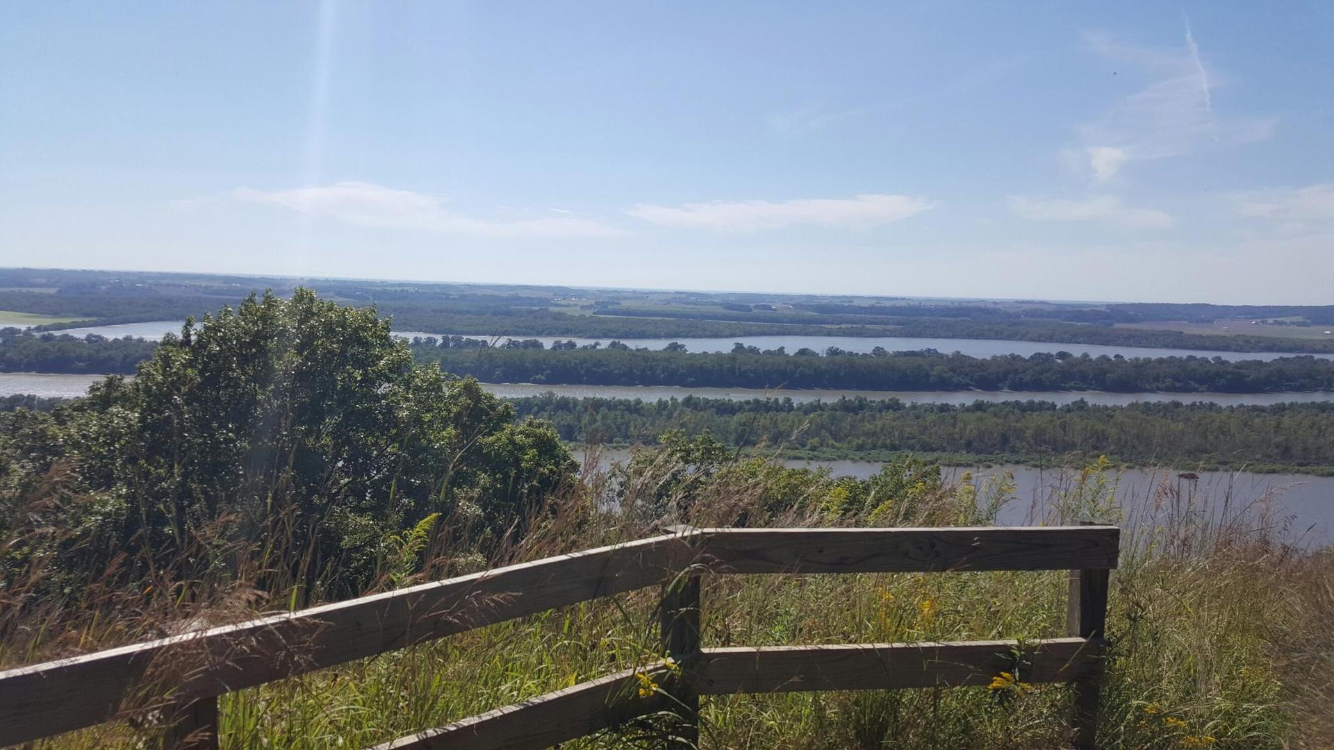 Sunny panoramic view of a wide river and distant landscape from behind a fence.