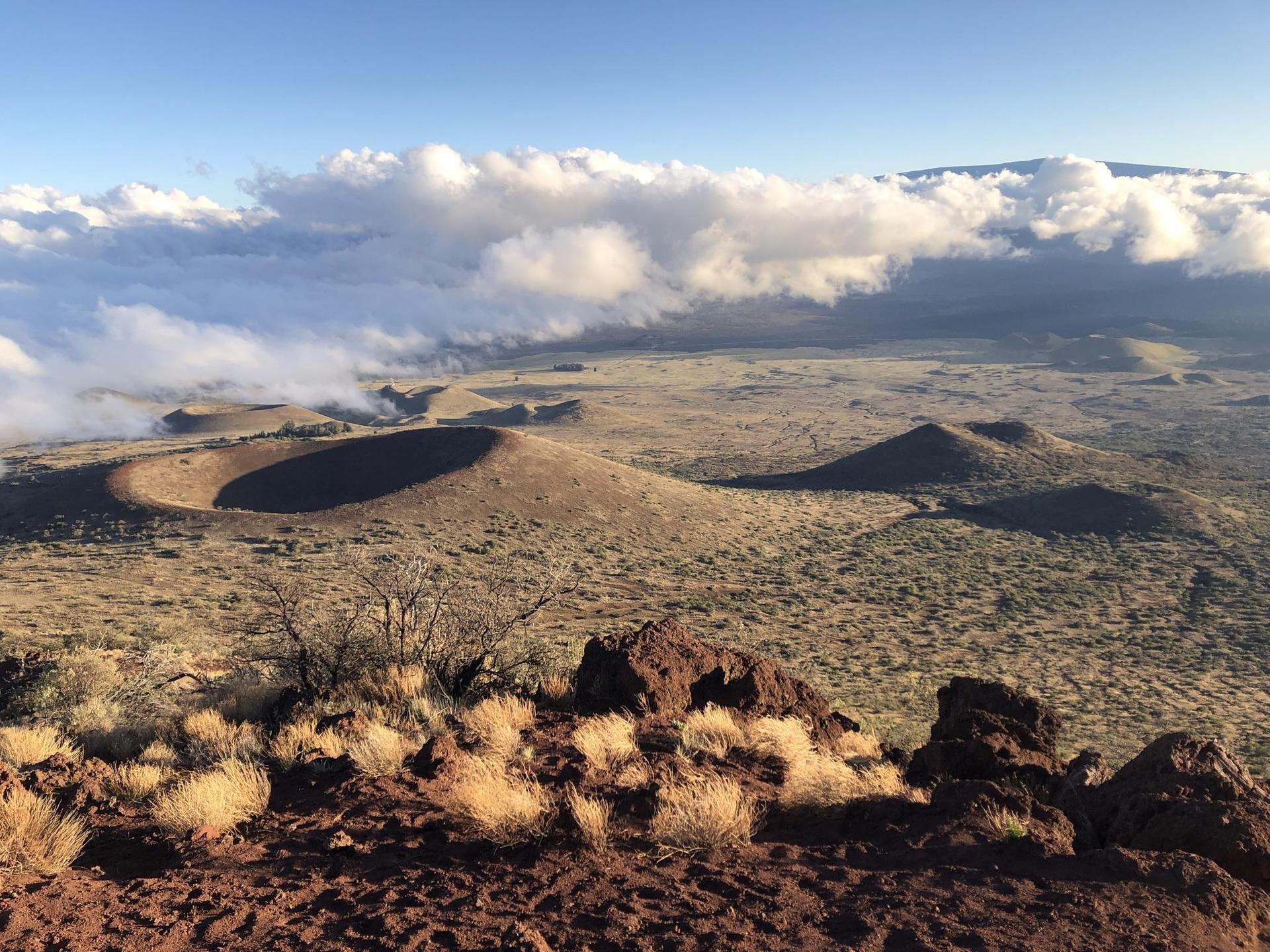 Aerial view of volcanic craters and dry landscape under a cloudy sky.