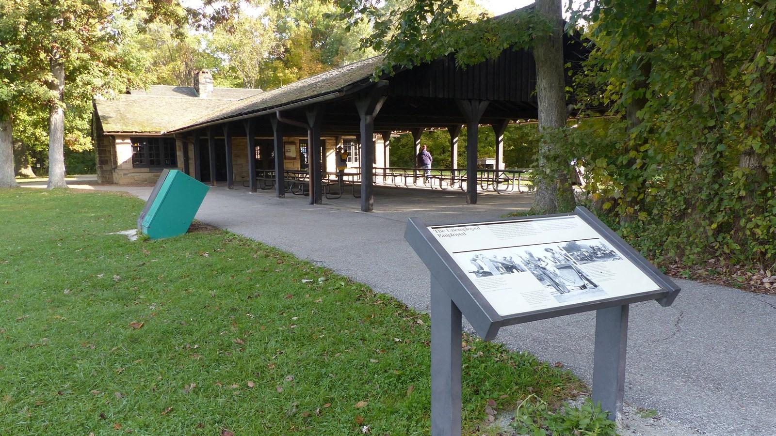 Informational sign near a stone building with a covered porch and people.
