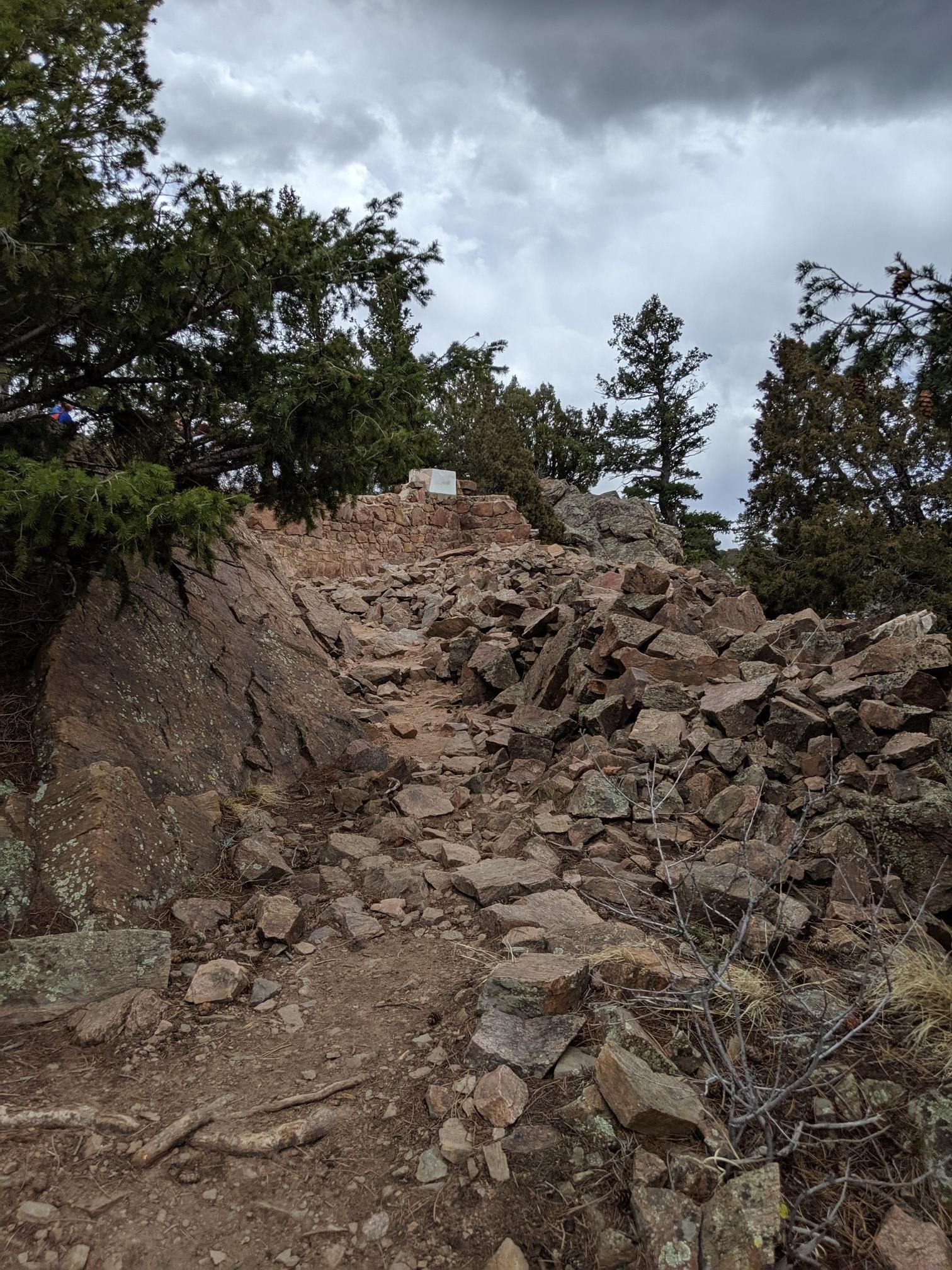 Steep, rocky uphill trail through rugged terrain with scattered trees.