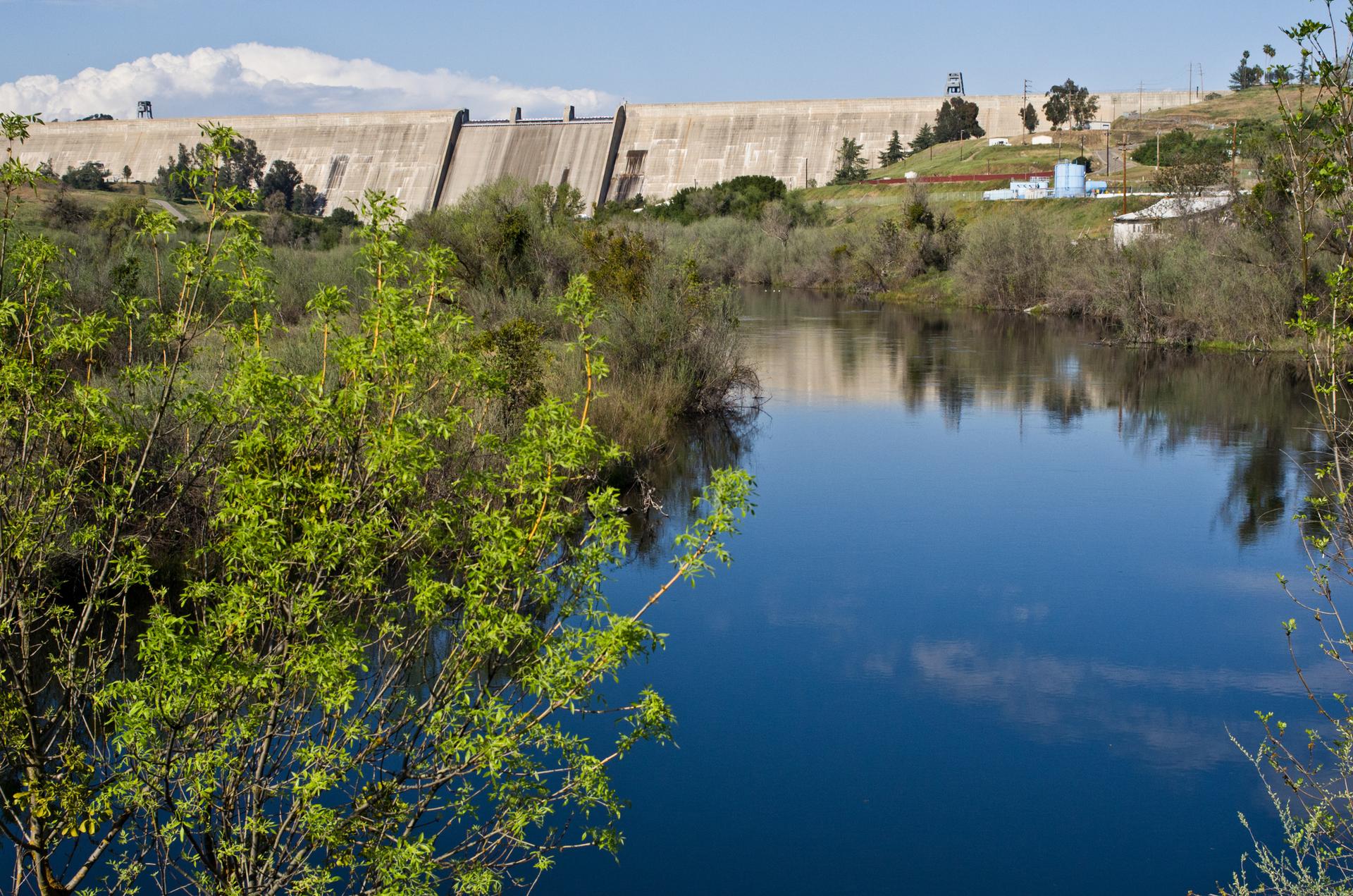 Calm blue water in front of a massive concrete dam under bright daylight.