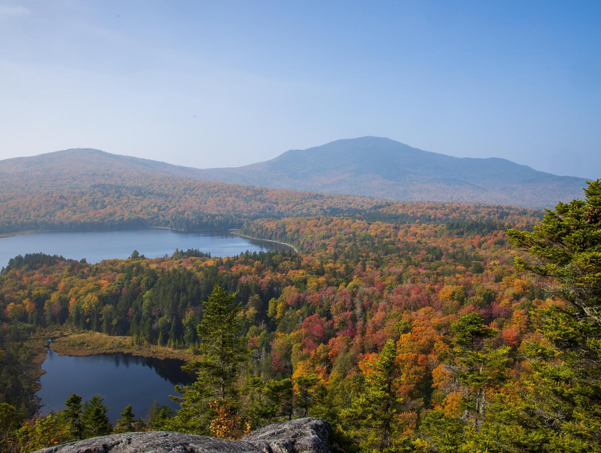 Panoramic view of two lakes surrounded by vibrant autumn forests and distant mountains.