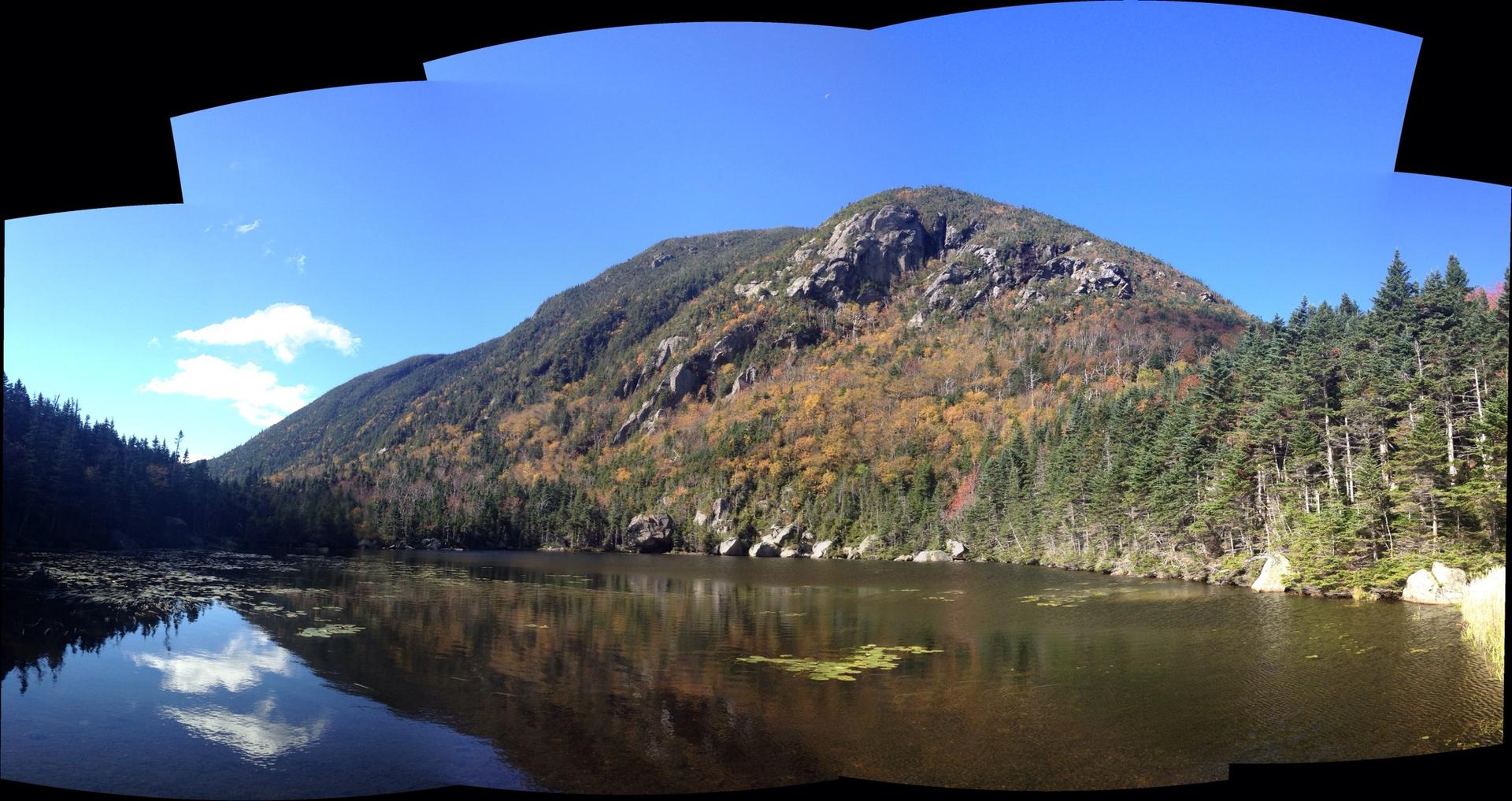 Panoramic view of a mountain reflecting in a calm lake under a clear sky.