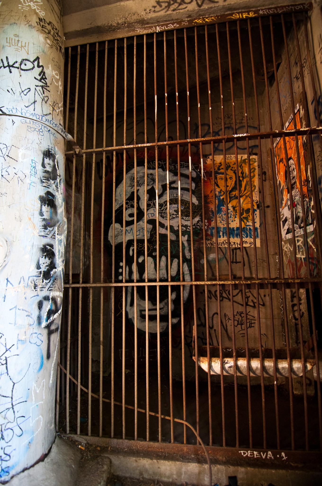 Dark, graffiti-covered concrete tunnel with a rusty metal gate.