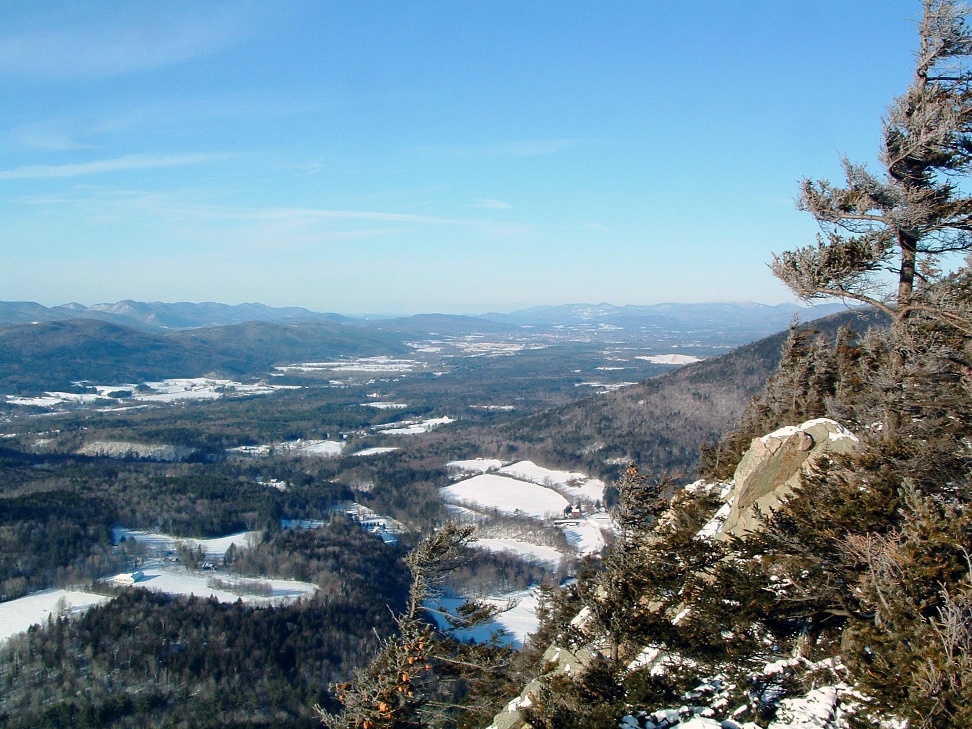 Winter panoramic view of snow-dusted valleys and forests from a rocky cliff.