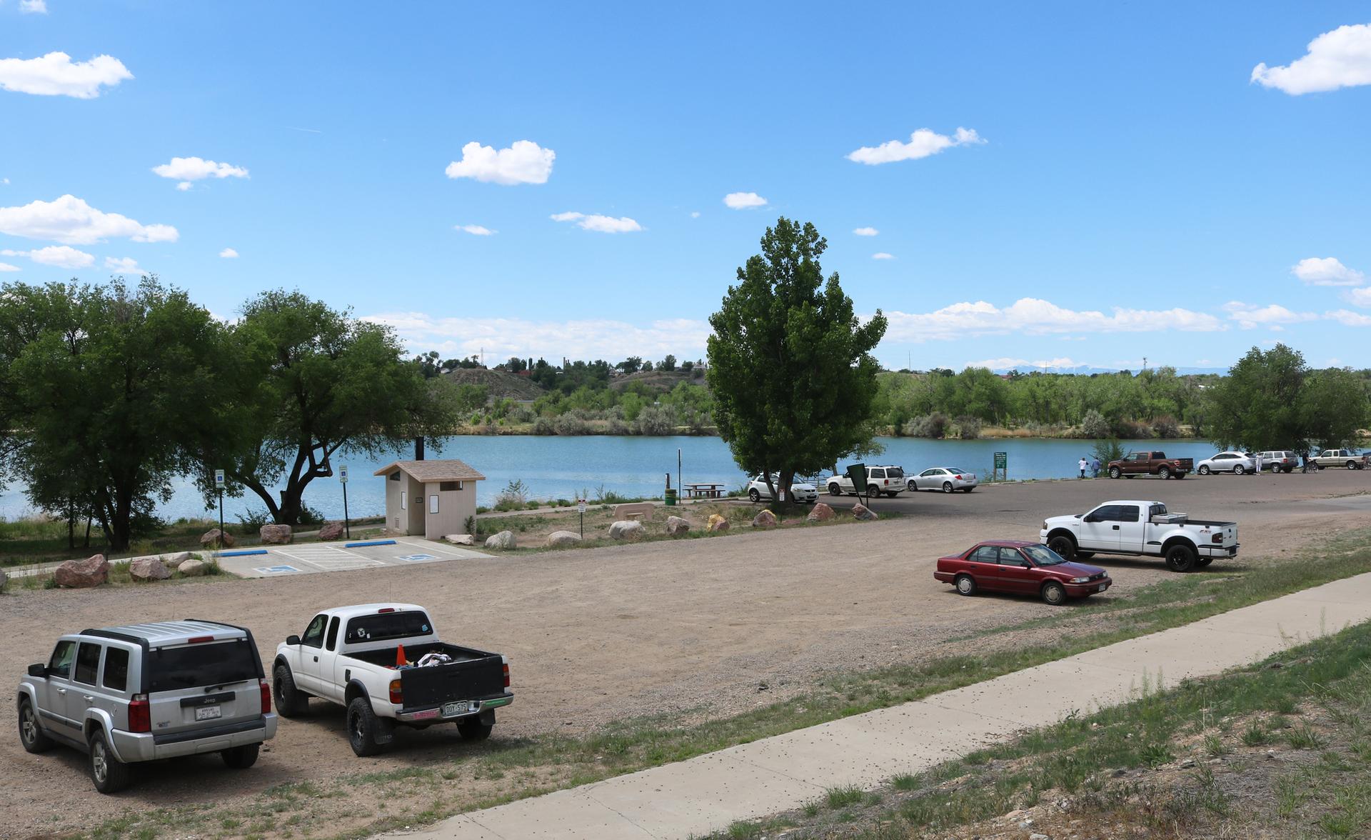 Vehicles parked on a dirt lot next to a wide river under a blue sky.