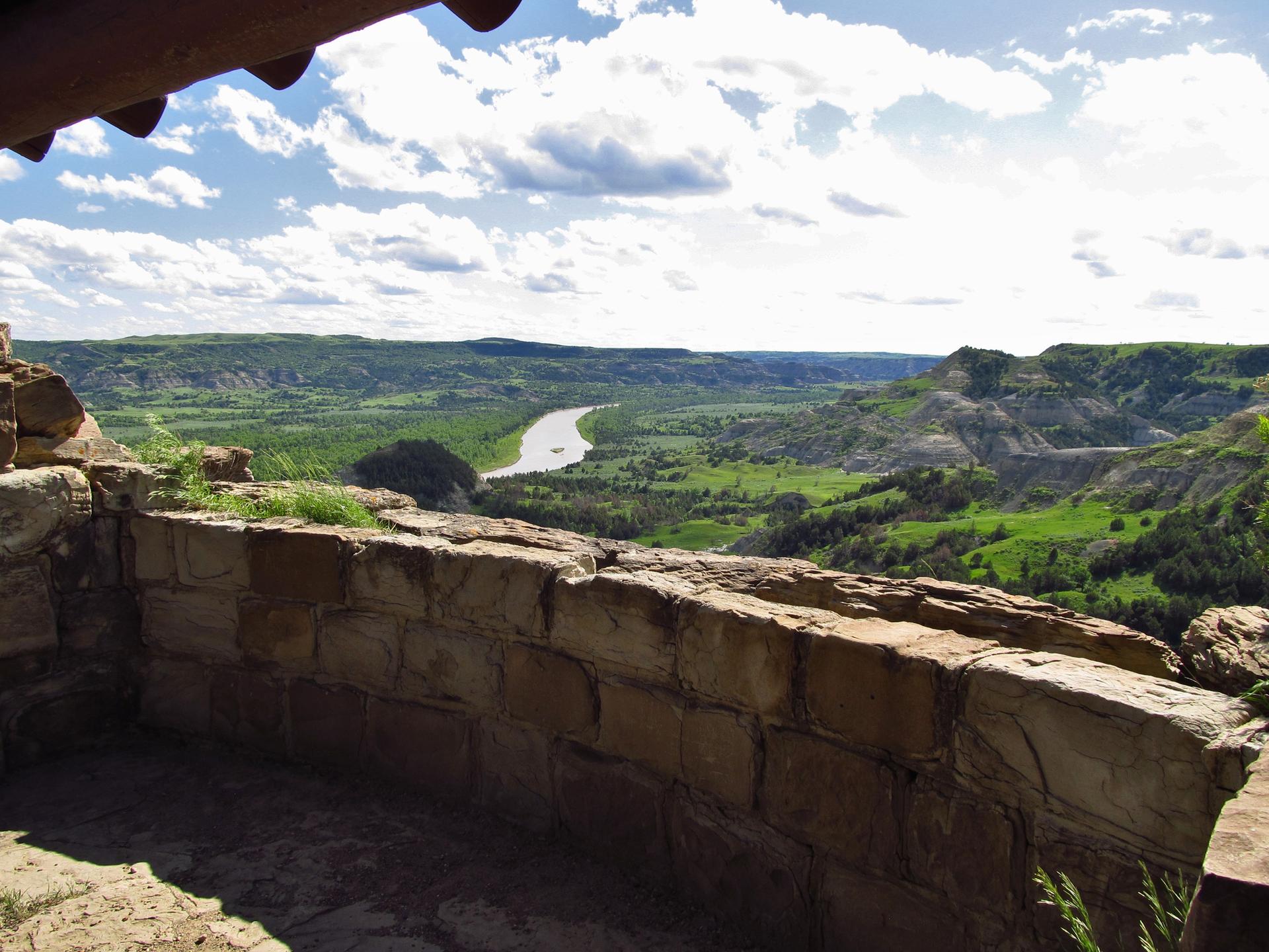 View from a stone wall overlooking a lush river valley under a cloudy sky.