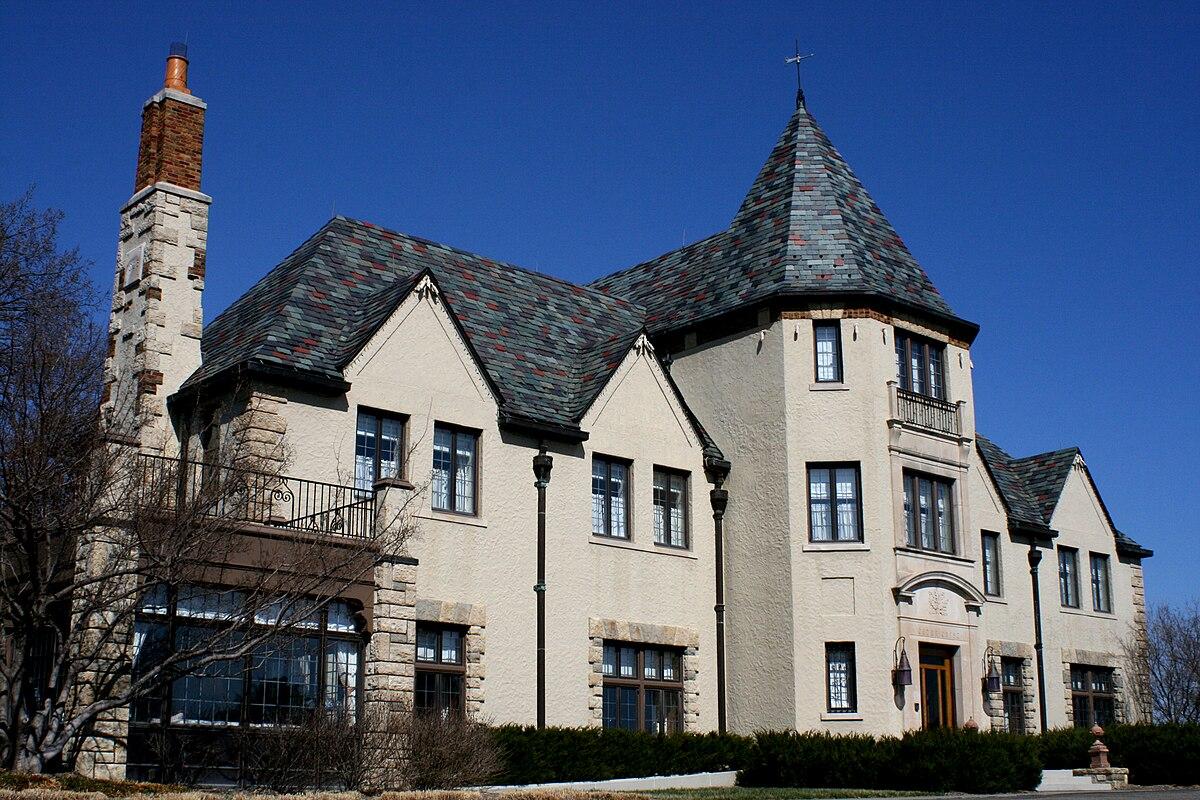 Ornate stone and stucco mansion with a tall chimney and turret under a clear blue sky.