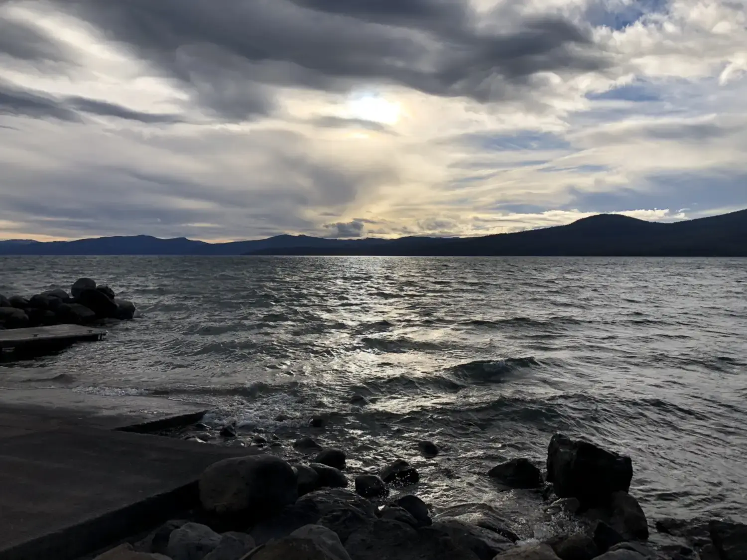 Dark, wavy lake under a dramatic cloudy sky with distant mountains.