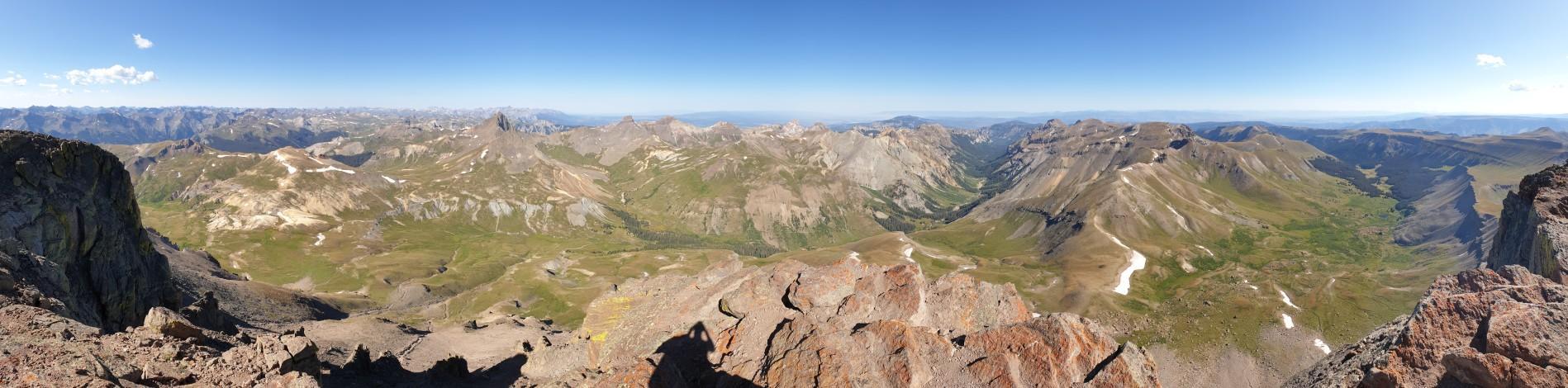 Panoramic view of expansive mountain ranges with green valleys under clear sky.