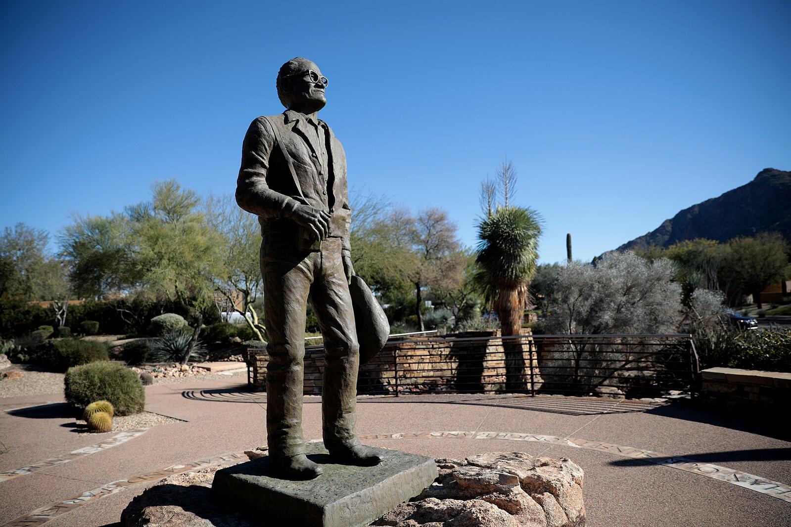 A bronze statue of a man in a desert landscape under a clear sky.