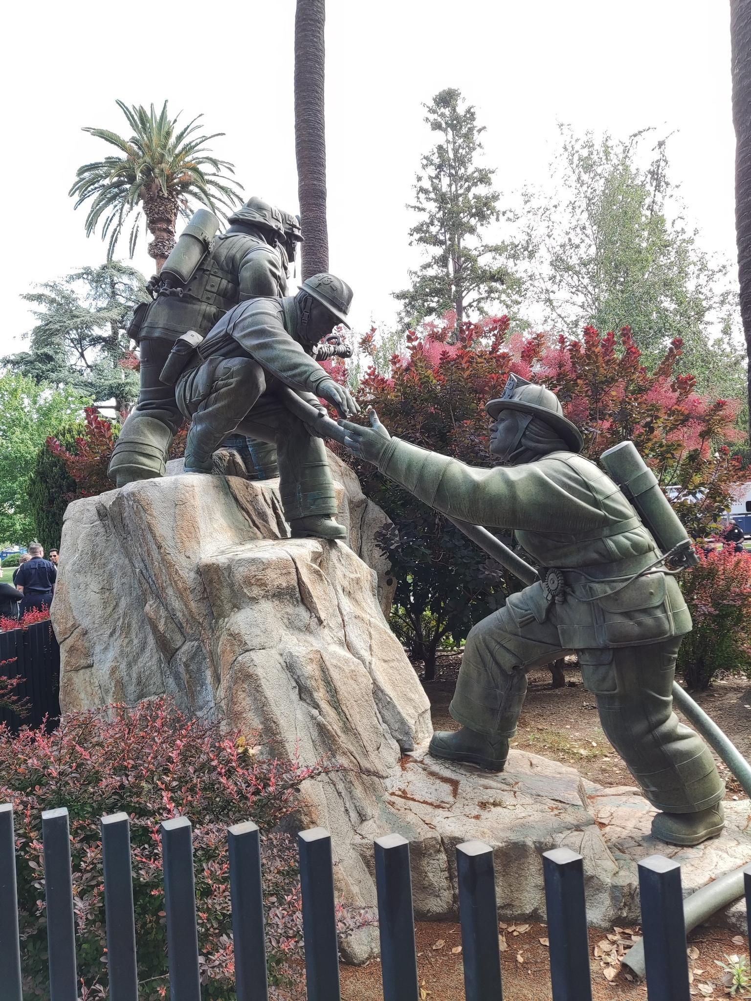 Bronze statue of three figures in firefighting gear on a rock.