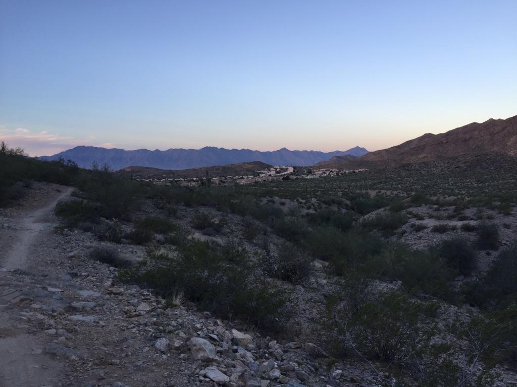 A wide desert landscape at dusk with distant mountains and a clear sky.