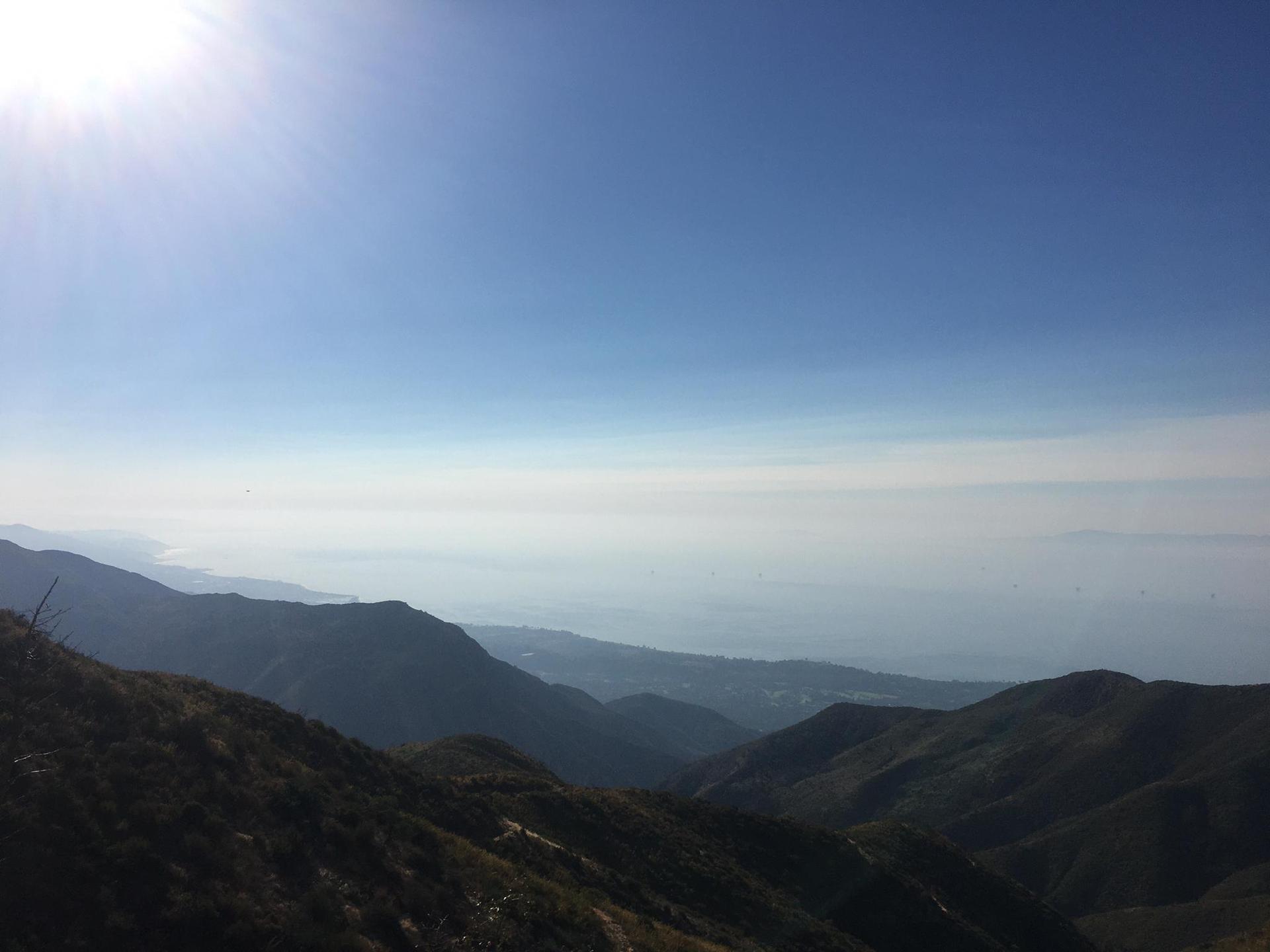 Bright sun over a vast mountain range with a hazy distant horizon.