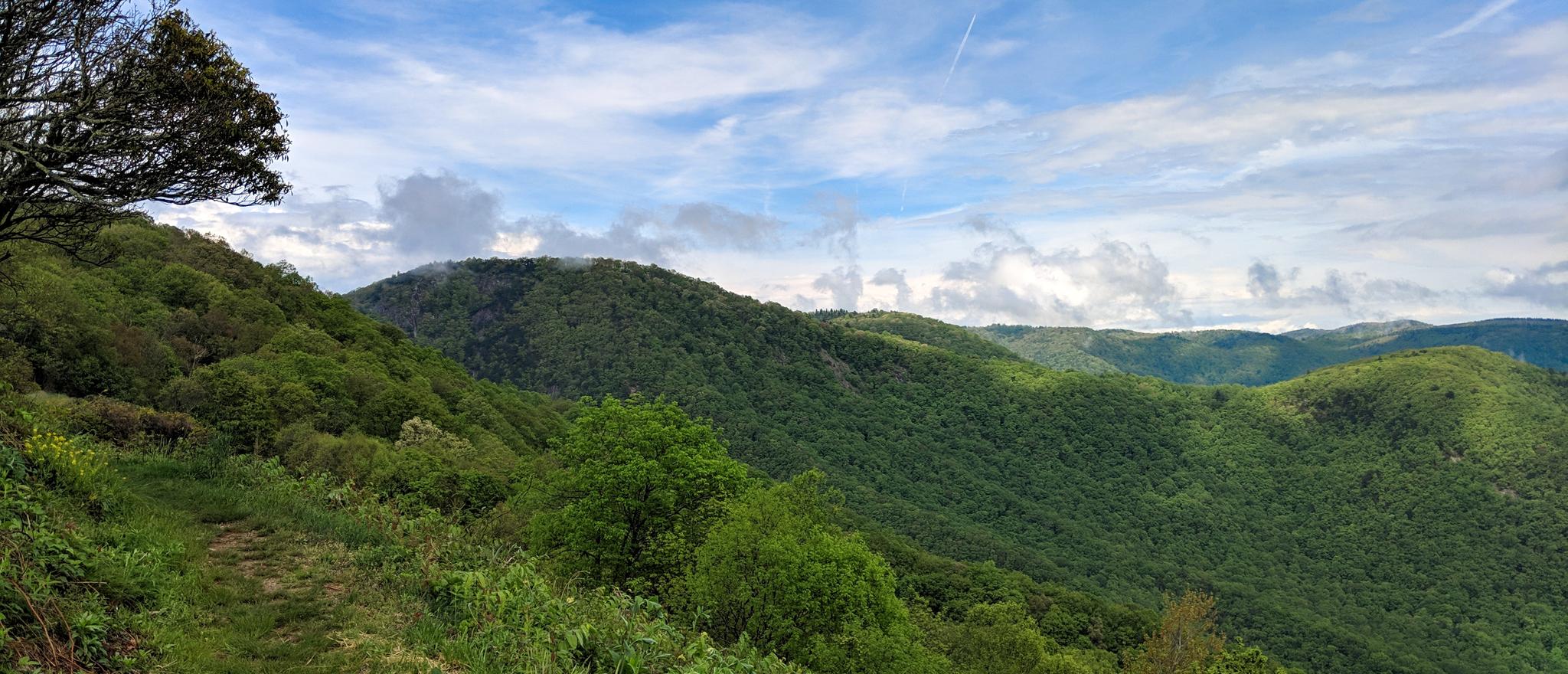Expansive view of lush green forested mountains under a partly cloudy sky.