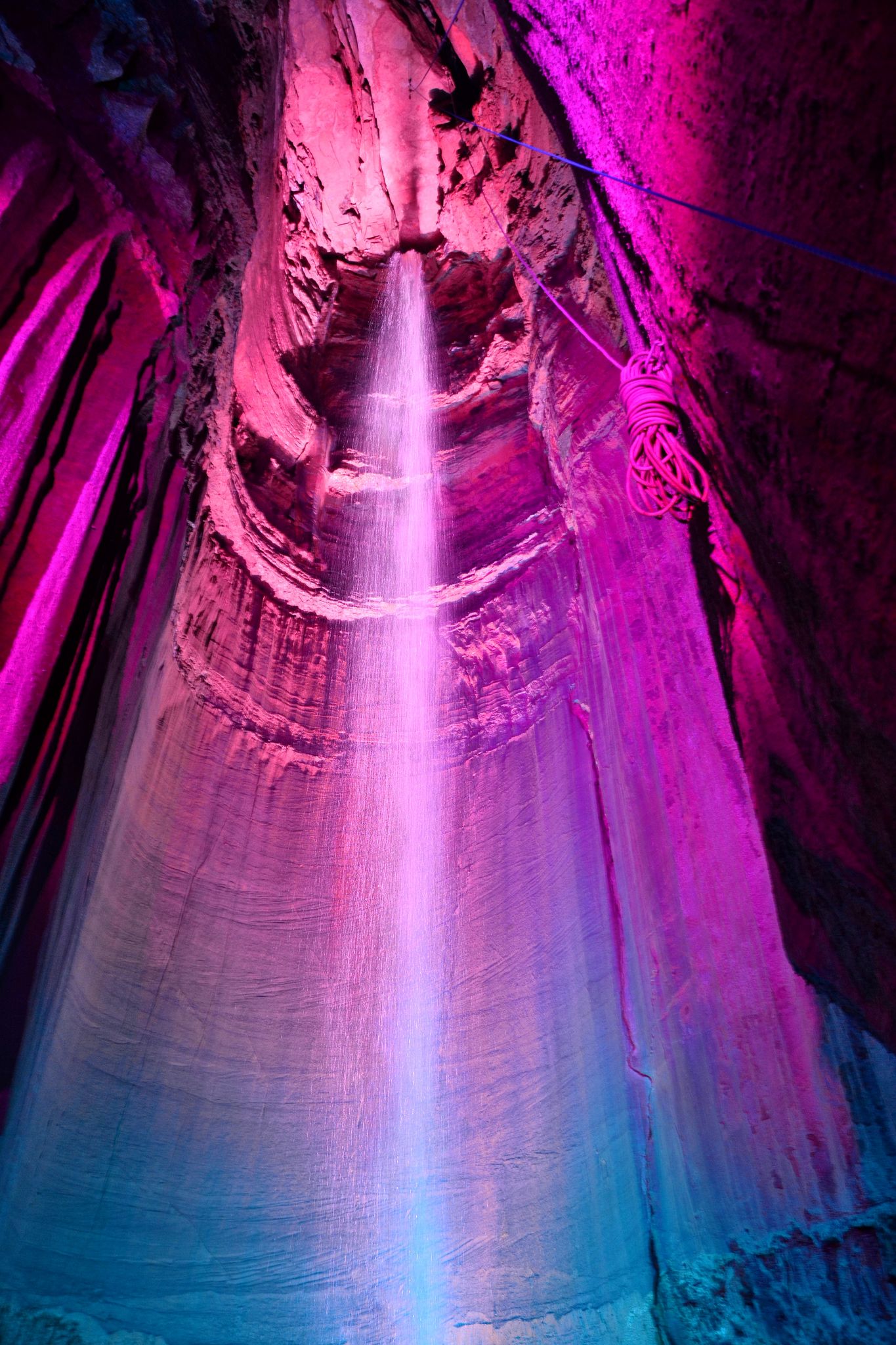 A waterfall cascades down a cave, illuminated by vibrant pink and blue lights. - Guild Hardy Loop Trail