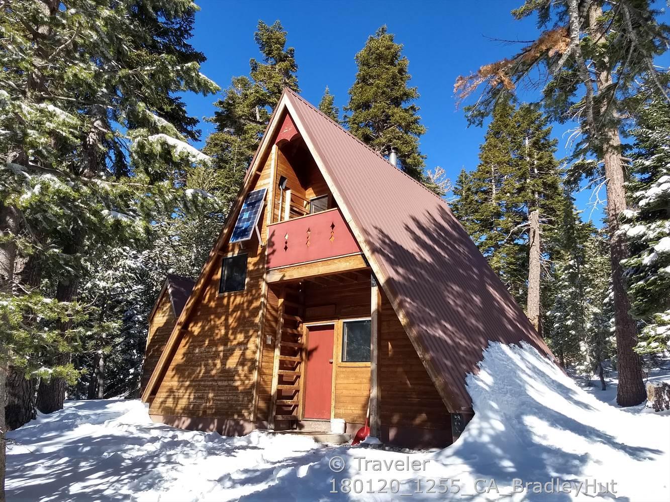 A-frame cabin in a snowy forest, bathed in bright sunlight.