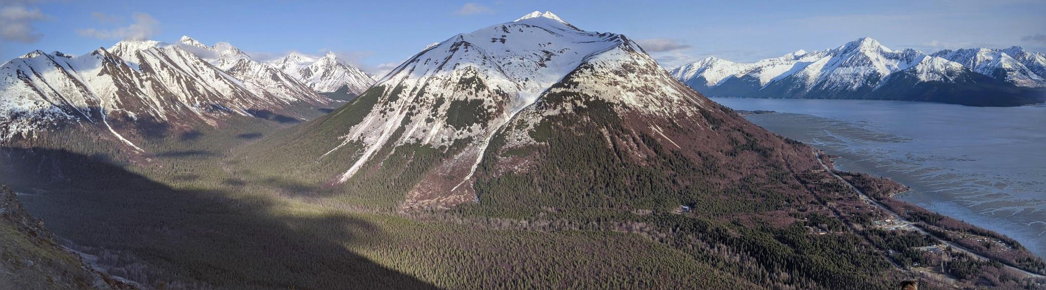Panoramic view of snow-capped mountains, forested valleys, and a large body of water.