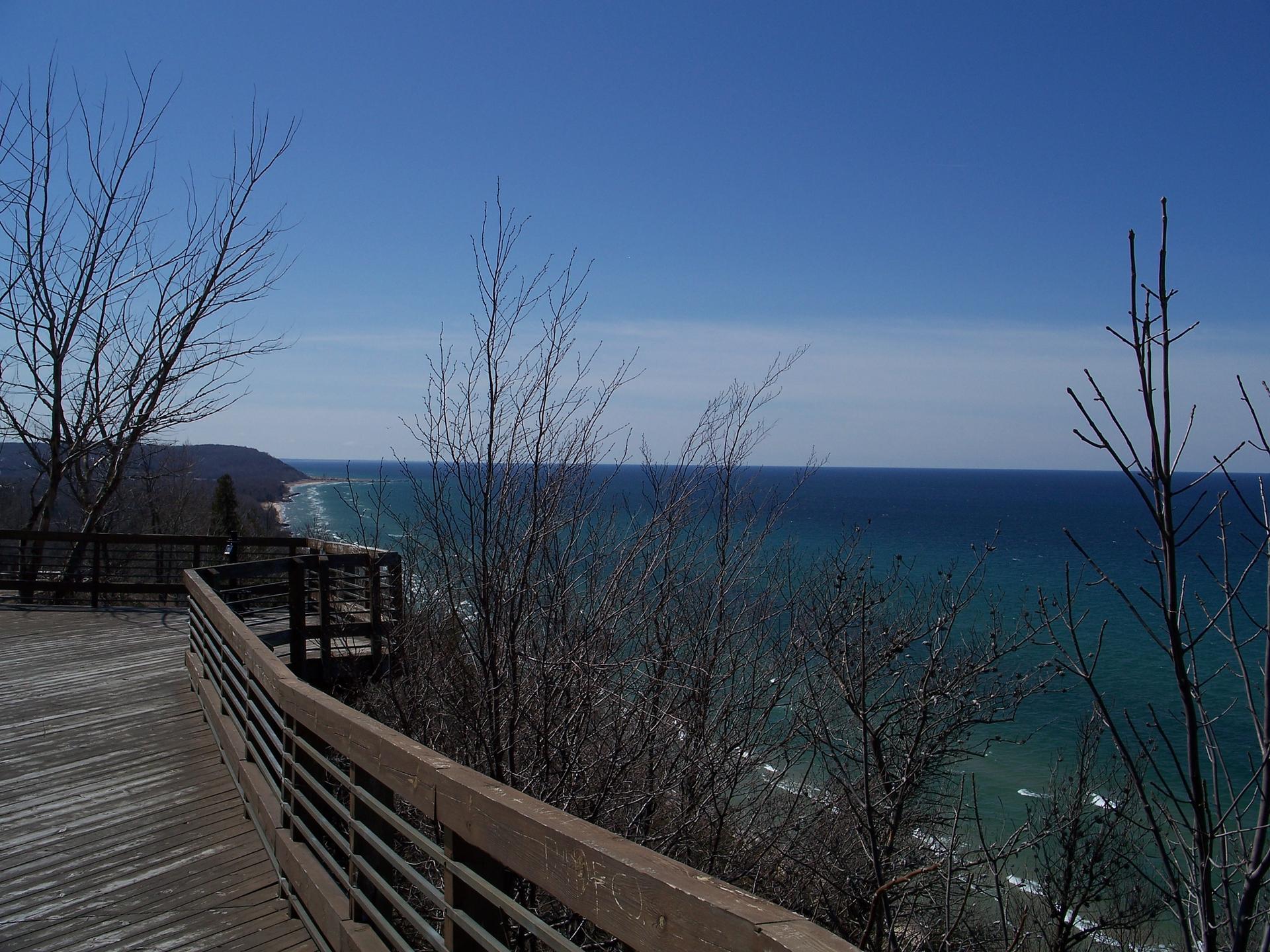 A wooden boardwalk offers a sunny view of a vast blue body of water.