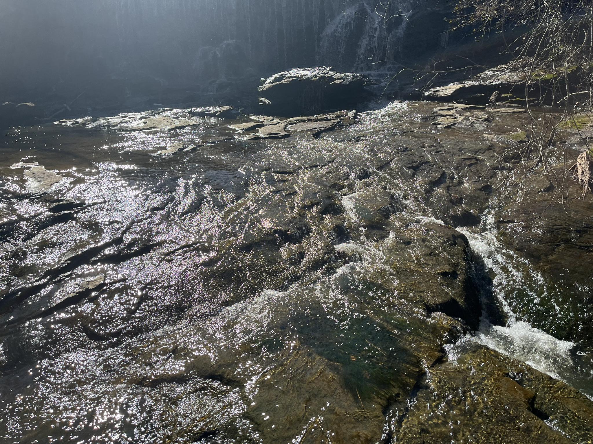 A rocky stream with flowing water, dappled with sunlight.