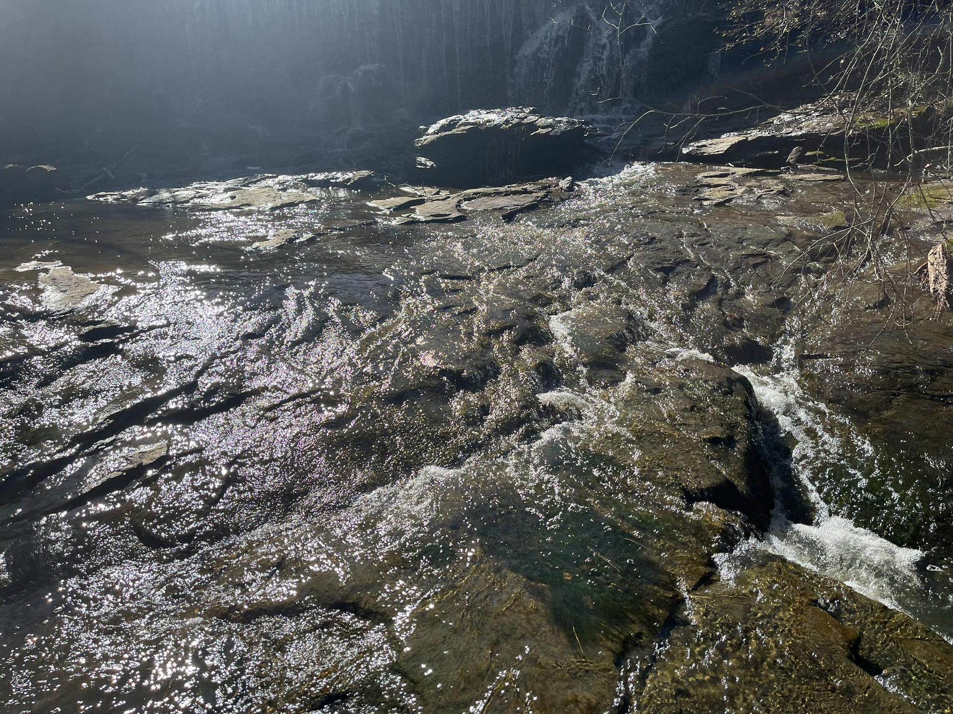 A rocky stream with flowing water, dappled with sunlight.