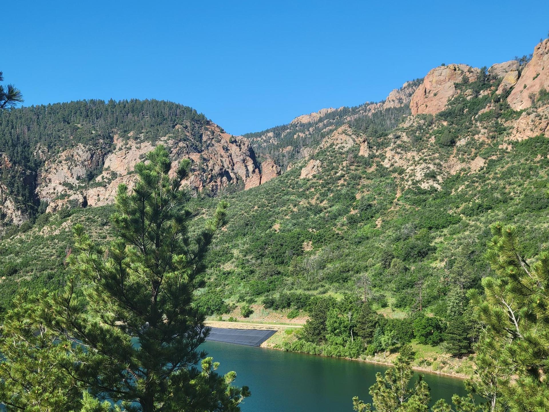 Sunny view of a lake nestled among green, rocky mountains with pine trees.