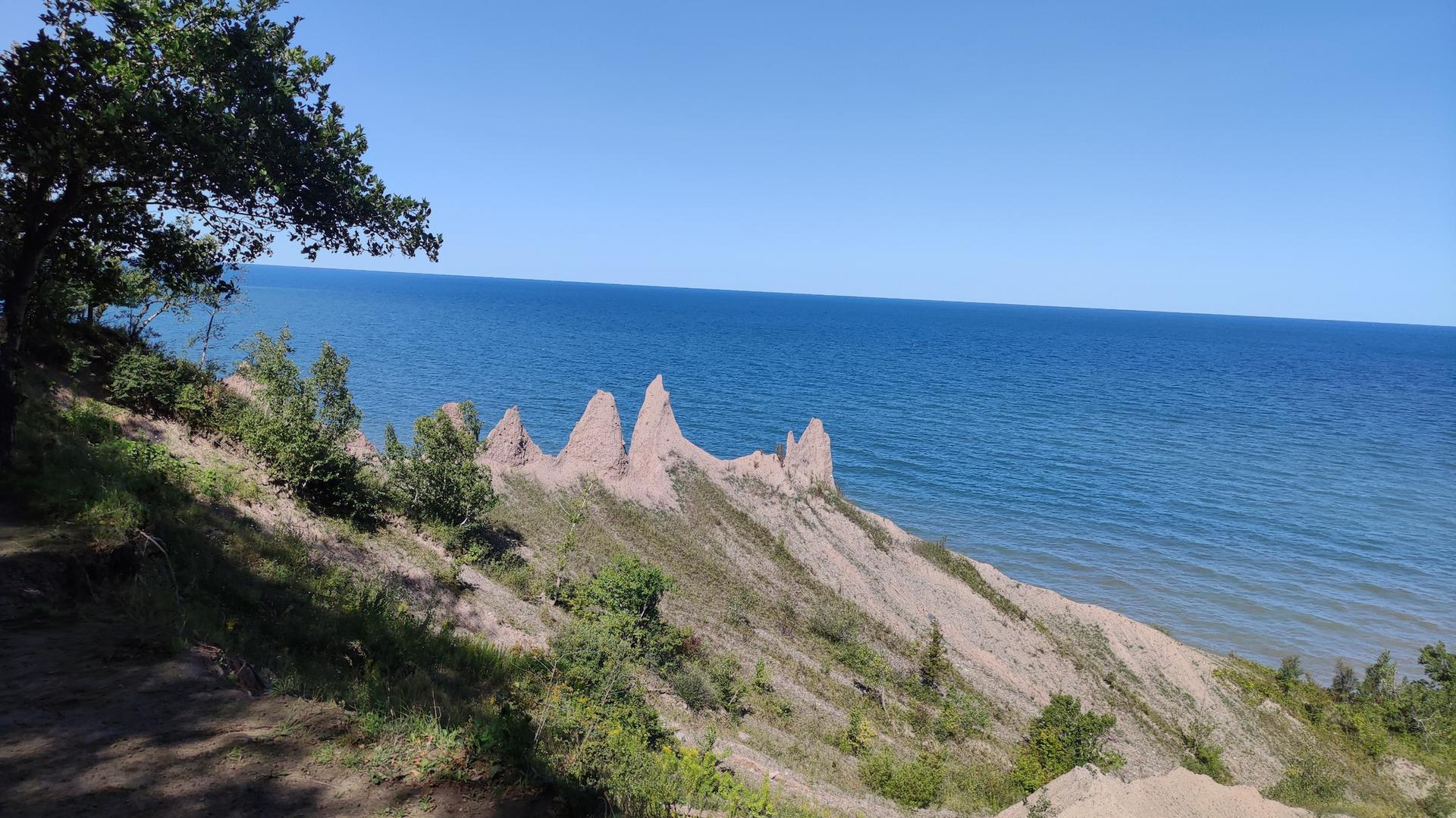 Sunny view of pointed, eroded cliffs beside a vast blue body of water.