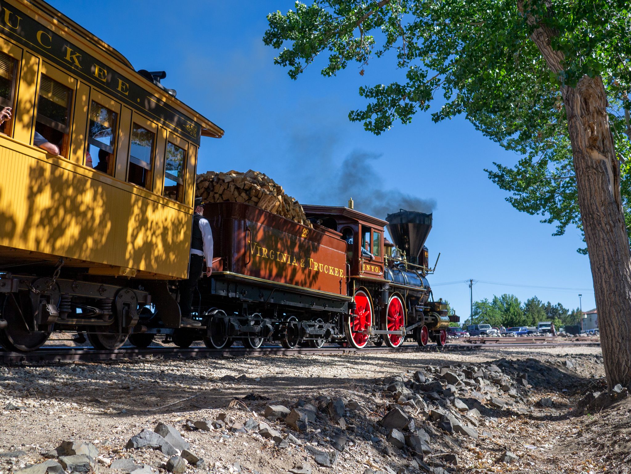 A vintage steam train with yellow and brown cars on tracks under a sunny sky. - Nugget Casino 💰💸 – Nevada State Railroad Museum loop from Corpus Christi Catholic Church