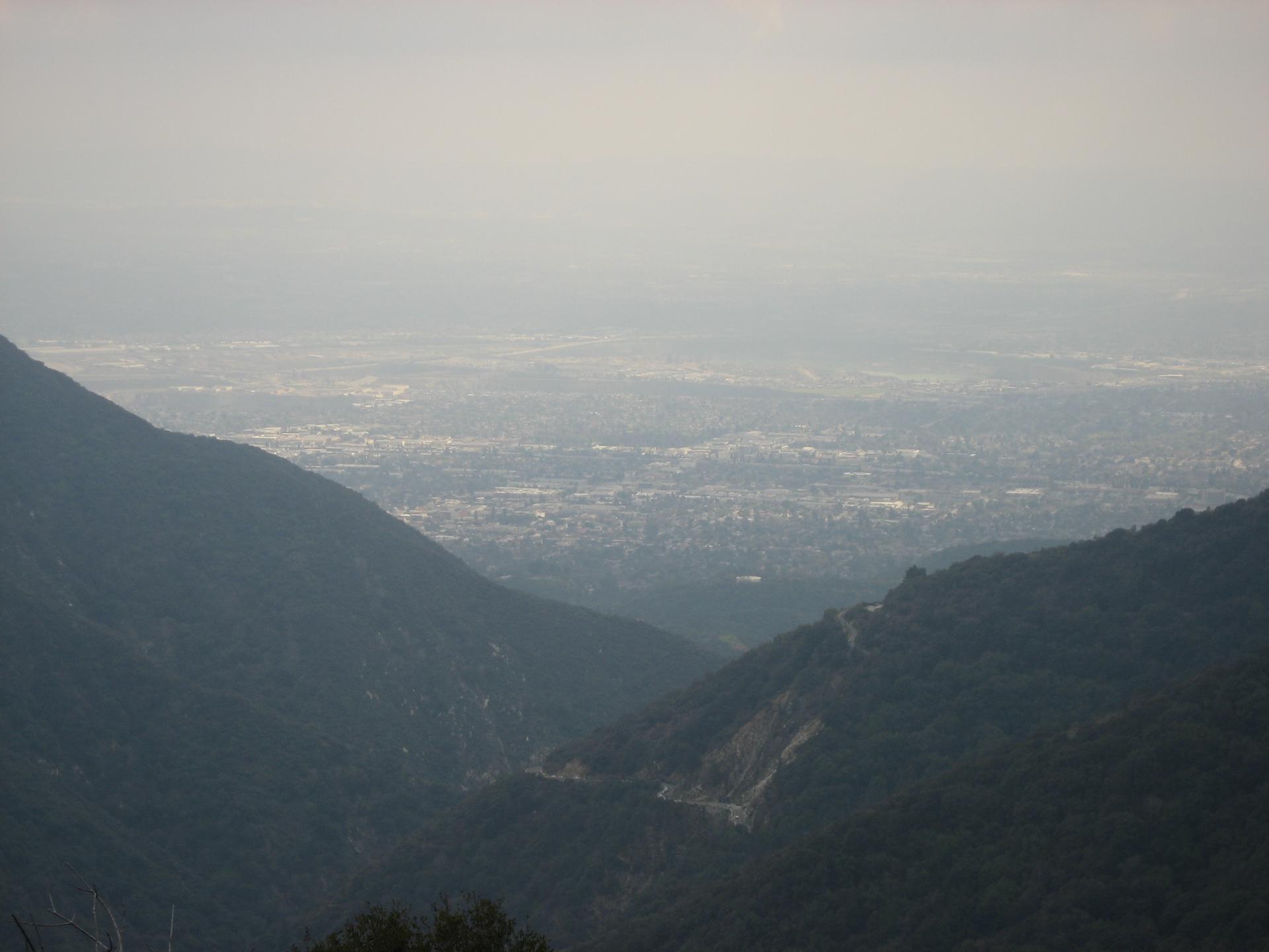 A hazy distant city view framed by two dark, forested mountain slopes.