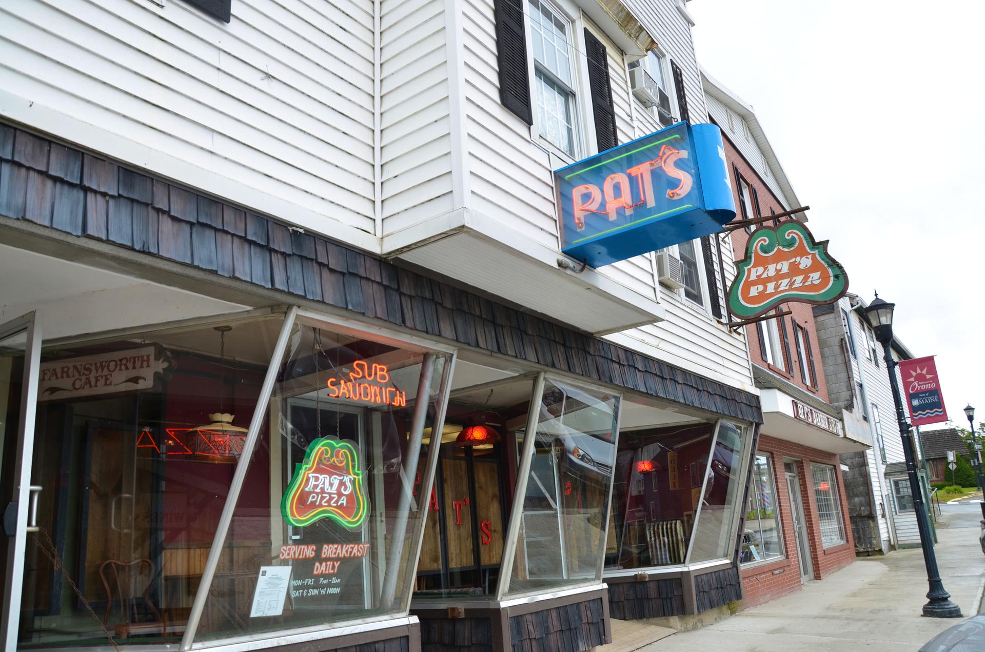 White clapboard building with a pizza shop and neon signs on an overcast day.