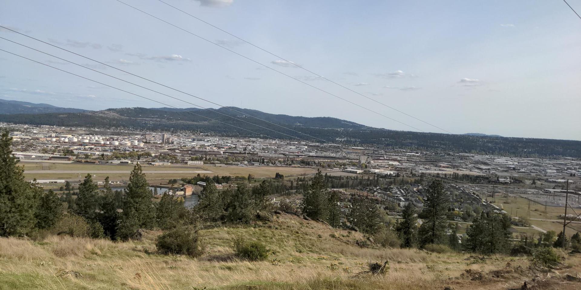 Overhead power lines stretch across a city nestled among distant hills.