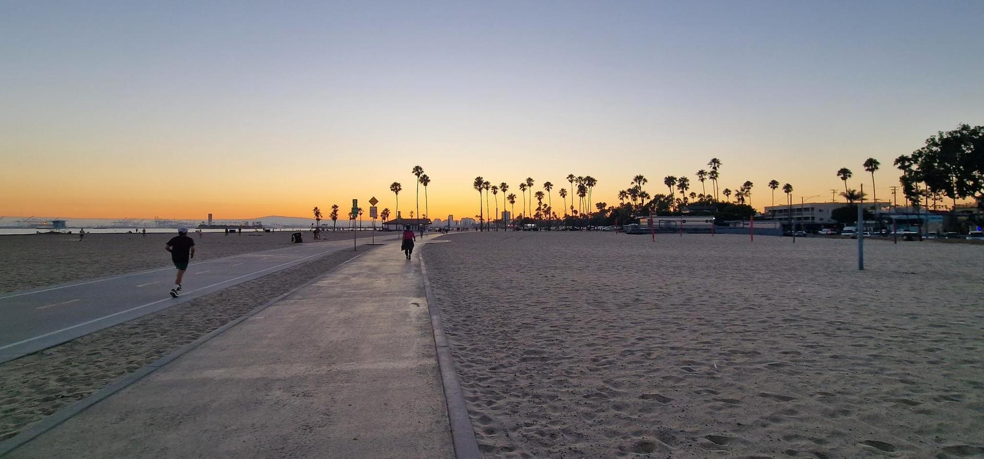 Wide sandy beach with palm trees and people walking at sunset.