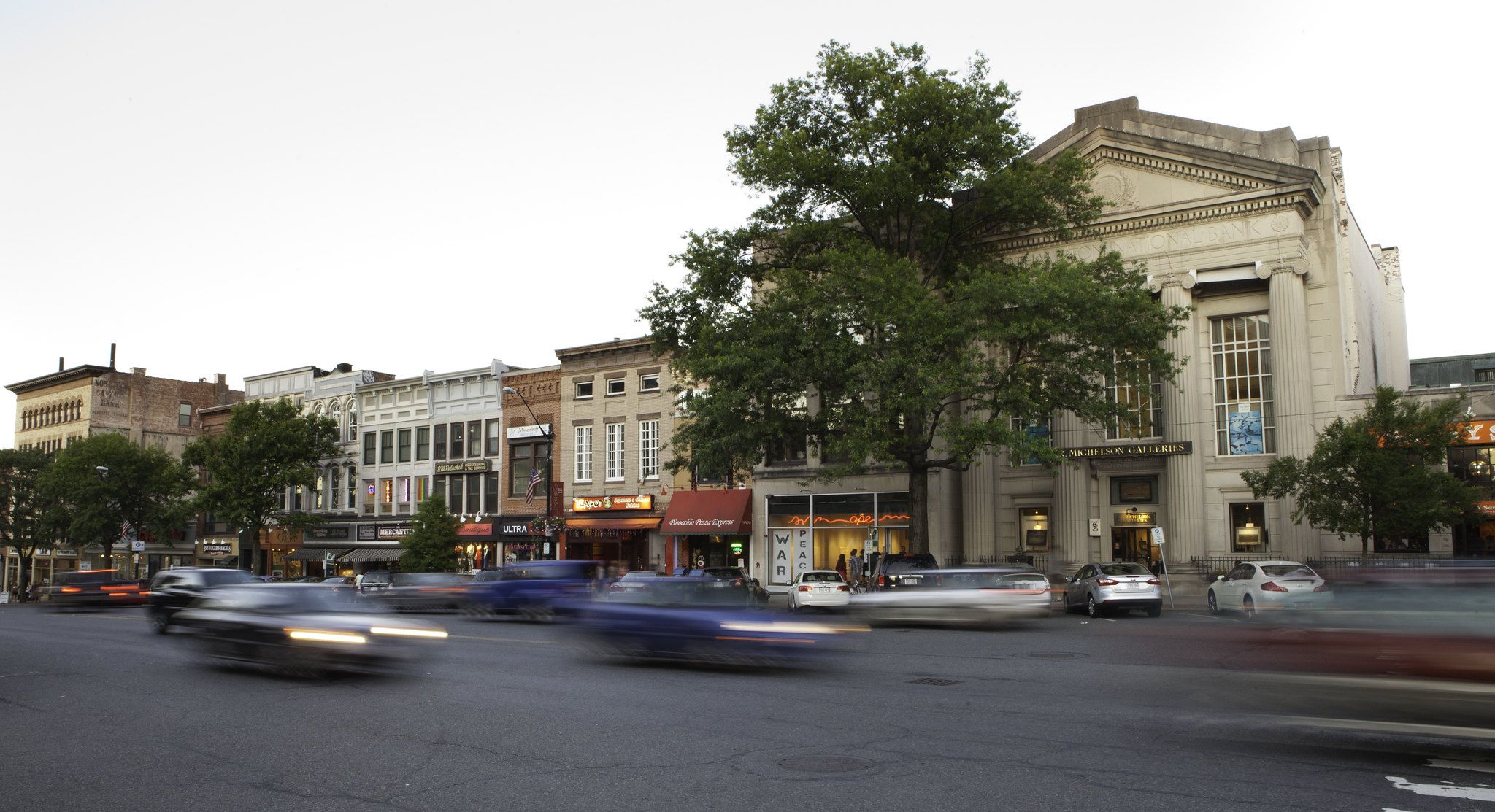 Busy city street with blurred cars and historic buildings at dusk. - Mass Central Rail Trail