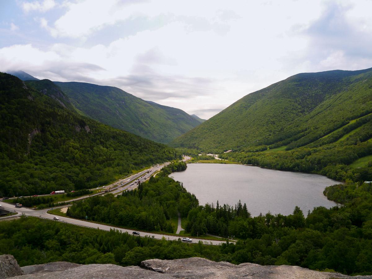 A lake and road wind through a vast, green mountain valley.