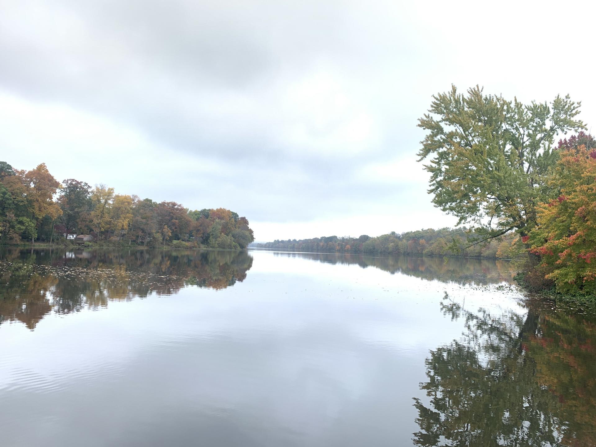 Wide river reflecting a cloudy sky, with autumn trees on distant banks.