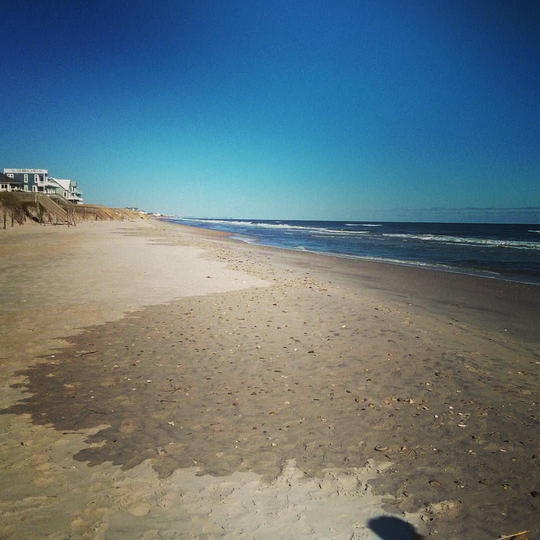 Expansive sandy beach with ocean waves and distant houses under a clear blue sky. - East Coast Greenway: Jacksonville to North Topsail Beach