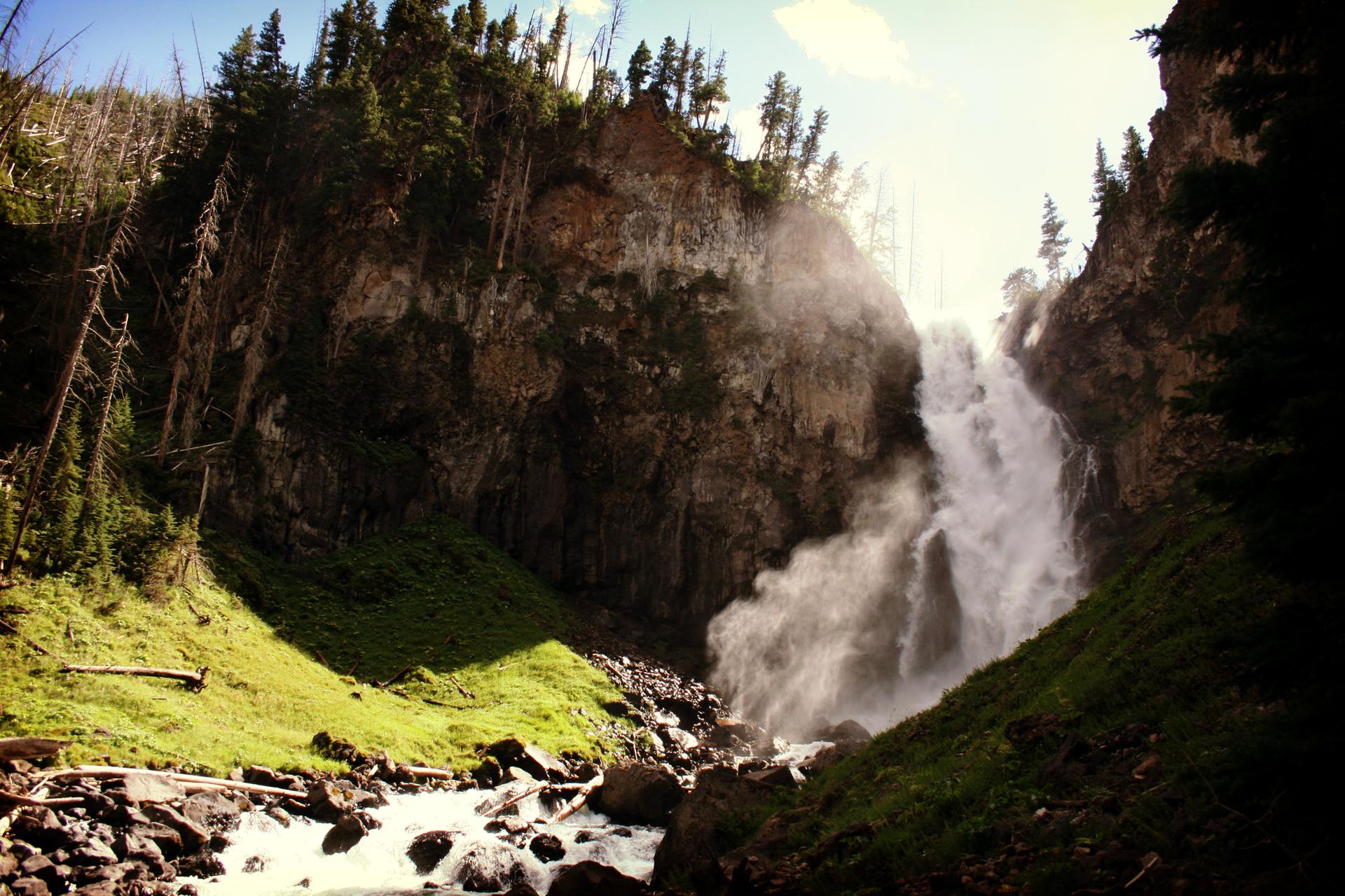 Powerful waterfall cascades down a rocky cliff into a sunlit, misty gorge.