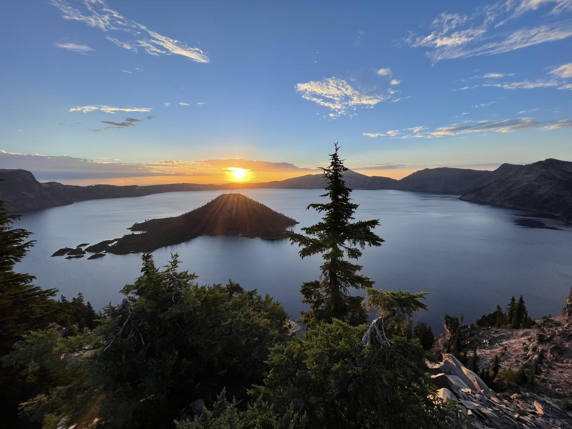 Golden sunset over a vast lake with a forested island, framed by dark trees.