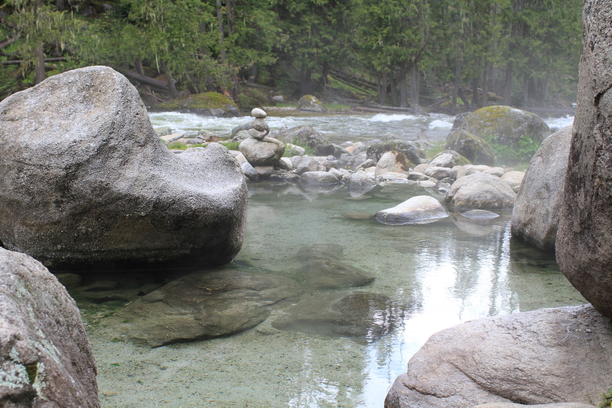 Clear, shallow hot spring pool with large rocks next to a flowing river. - Jerry Johnson Hot Springs