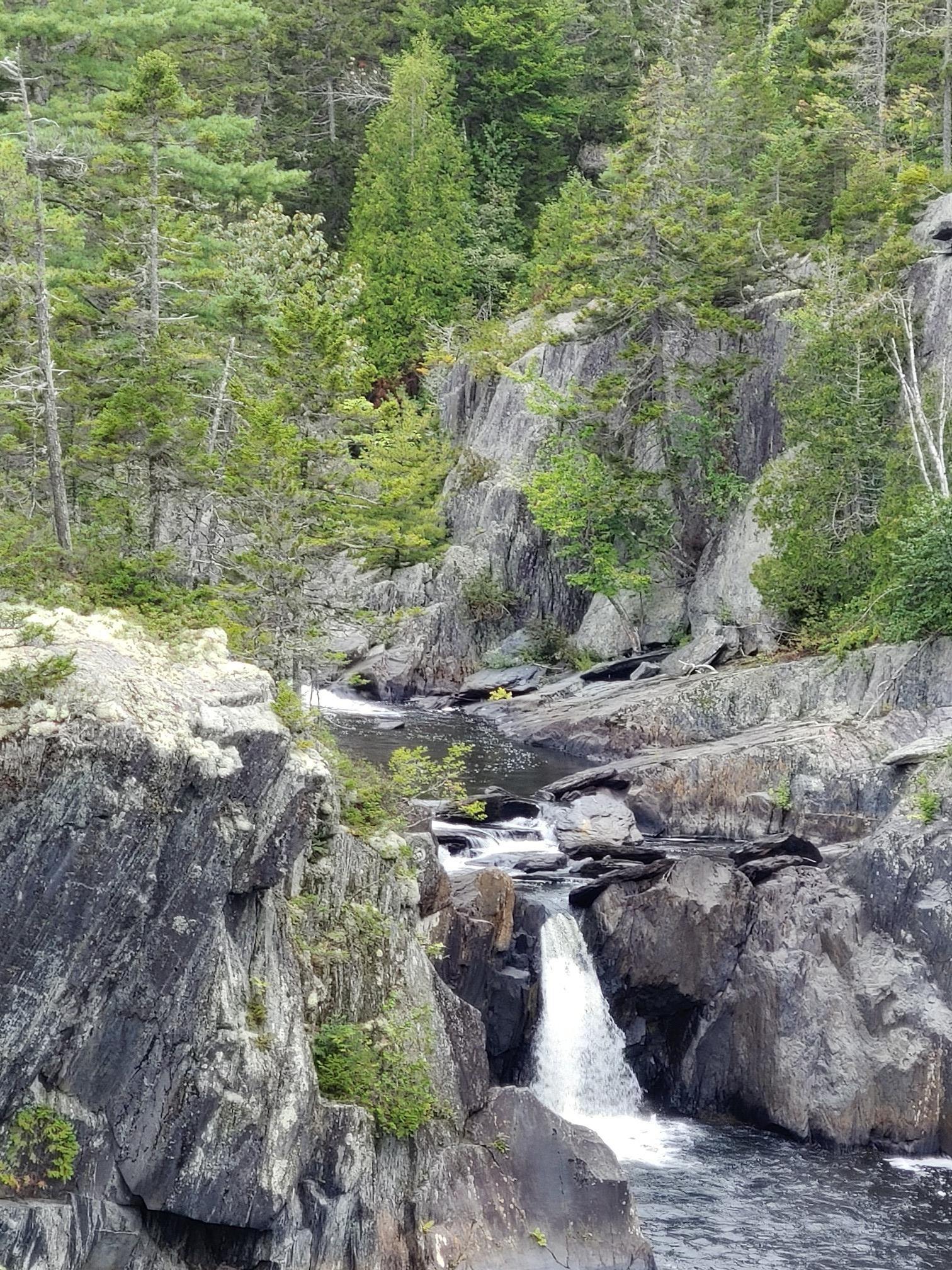 A waterfall cascades into a rocky river gorge surrounded by dense green forest.