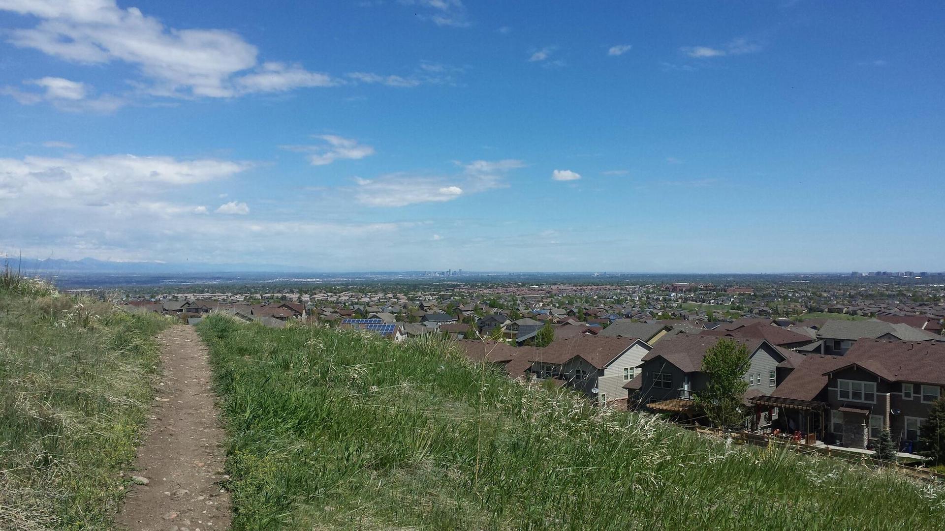 Grassy path overlooking a town with houses under a bright blue sky.