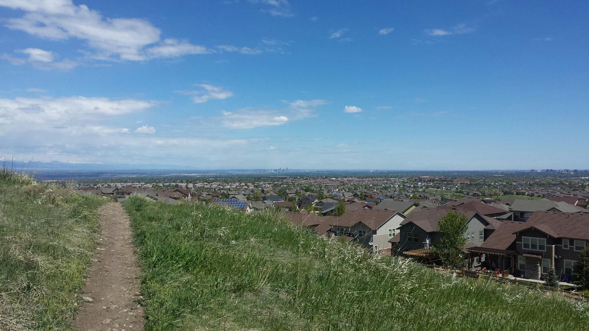 Grassy path overlooking a town with houses under a bright blue sky. - East/West Regional Trail and Dad Clark Trail Loop