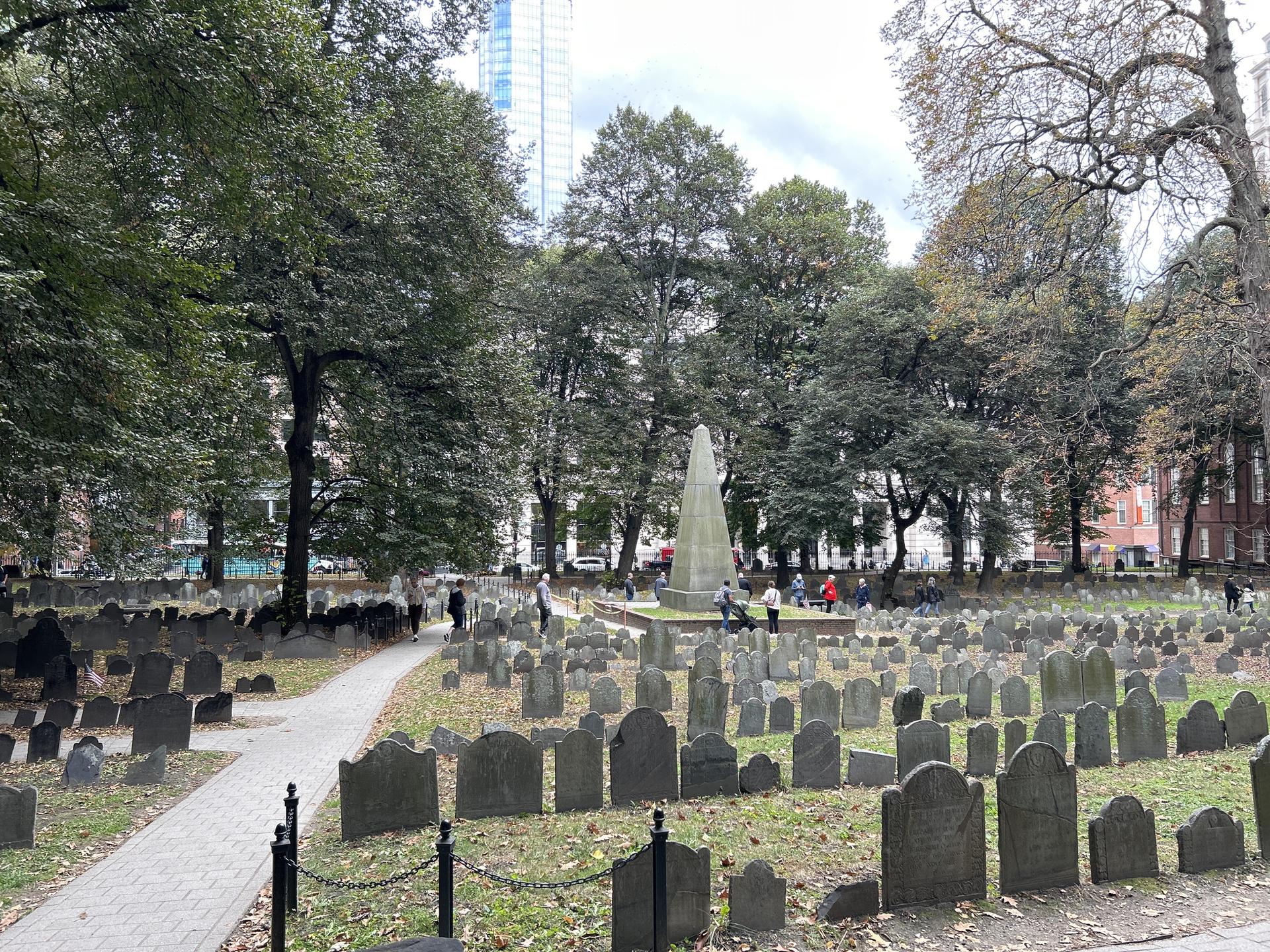 Historic cemetery with many headstones, tall monument, and green trees.