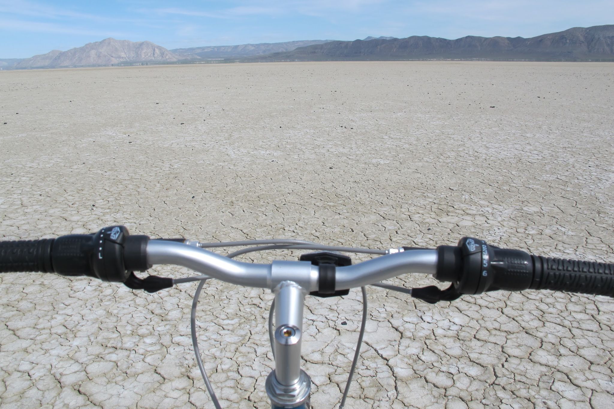 Bicycle handlebars over a vast cracked dry lakebed under a bright sky. - Trego Hot Springs via Black Rock Desert