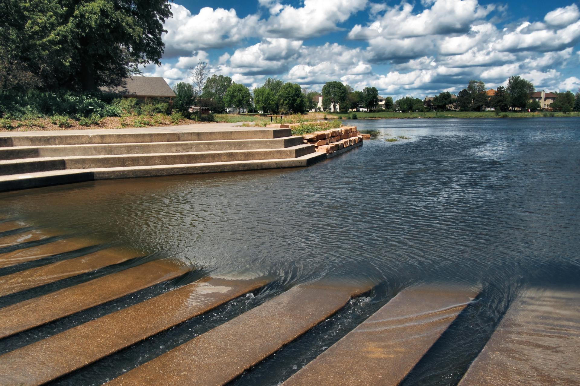 Concrete steps descend into rippling water under a bright, cloudy sky.