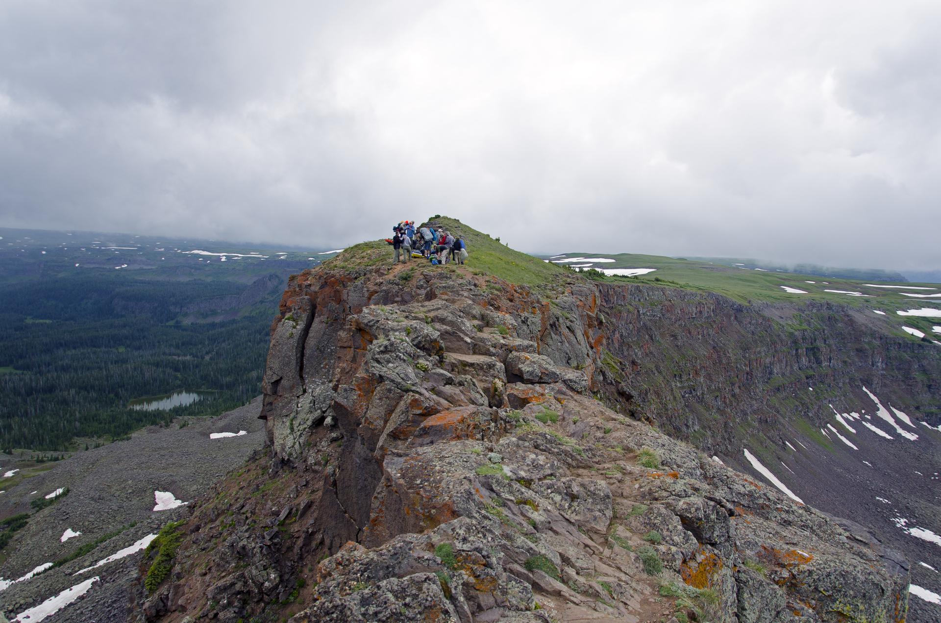 Group of hikers stand on a rocky mountain ridge under a cloudy sky.
