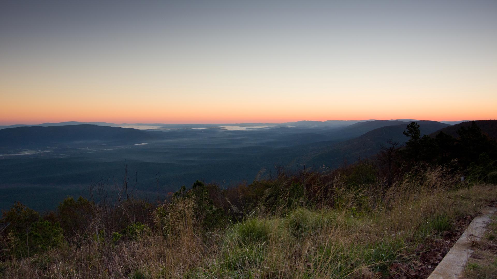 Panoramic view of misty valleys and rolling mountains under a colorful dawn sky.